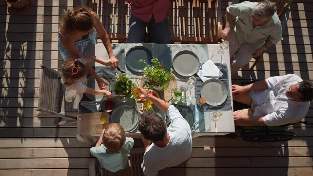Top view of 3 generations family eating at barbecue party dinner on patio, people sitting at table on patio with grill.