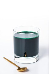 Spirulina drink in a glass with a spoon on a white background.