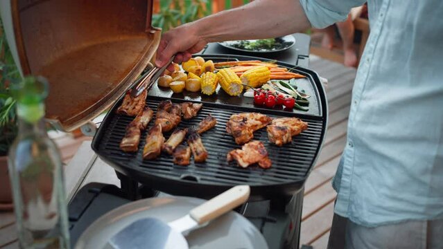 Unrecognizable man grilling ribs and vegetable on grill during family summer garden party, close-up
