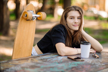 Portrait of pretty teenager girl with a skateboard is sitting and resting on the bench outdoors the skater park