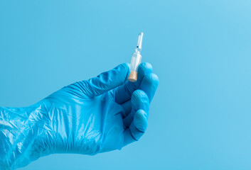 Medical glove. An ampoule with a white liquid in his hand in a blue medical glove. Isolated on a blue background.