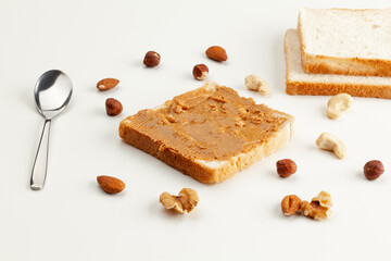 Square bread for toast with peanut butter. Nuts, spoon, bread slices and a peanut butter sandwich...