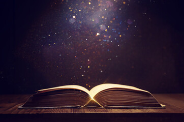 image of open antique book on wooden table with glitter overlay
