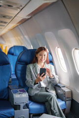 portrait of A successful asian businesswoman or female entrepreneur in formal suit in a plane sits in a business class's seat and uses a smartphone during flight