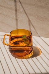 Mint tea in an orange glass mug on a light stone table with shadow stripes. Front view
