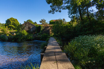 Old stone footbridge over the Neiva River in Antas, Esposende, Portugal with an old Azenhas, ancient mills, in the background.