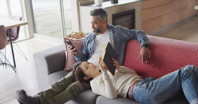 Happy diverse couple sitting in living room with book and smartphone