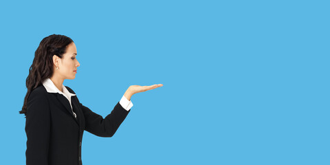 Profile side of beautiful businesswoman showing something or copy spase for product. Brunette woman looking at her hand in business studio concept, isolated against blue color background.