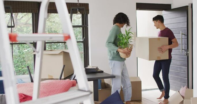 Happy diverse male couple moving house, carrying boxes and smiling