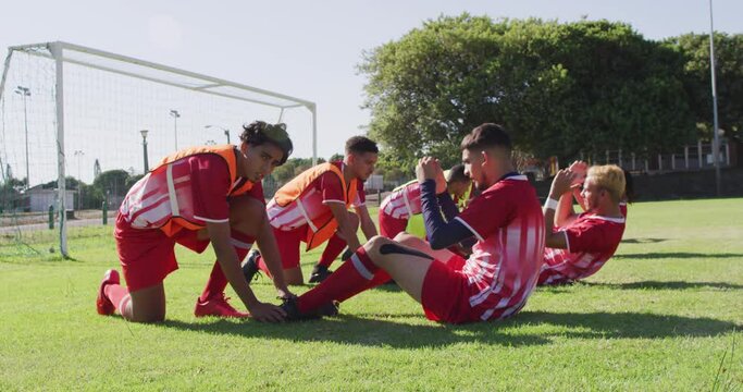 Video of diverse group of male football players warming up on field,doing sit -ups