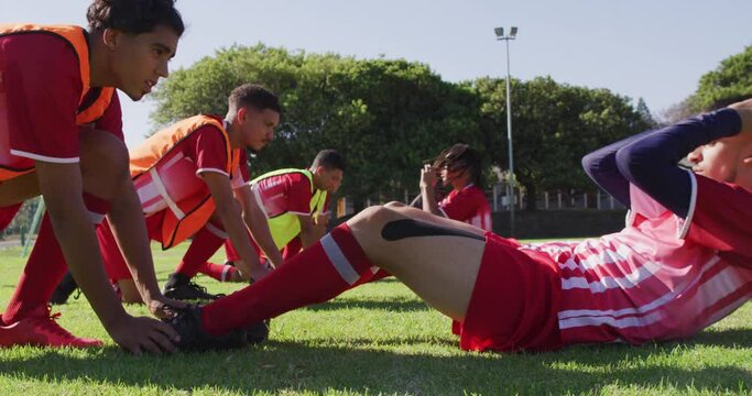 Video of diverse group of male football players warming up on field, doing sit-ups