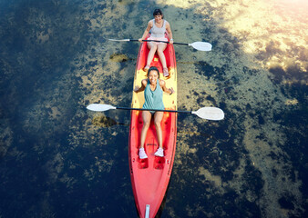 Above view of two smiling friends kayaking on the ocean together over summer break. Portrait of happy women canoeing and bonding outside in nature with water activity. Having fun on a kayak - obrazy, fototapety, plakaty
