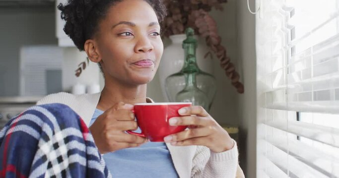Video of thoughtful african american woman drinking coffee and looking outside window