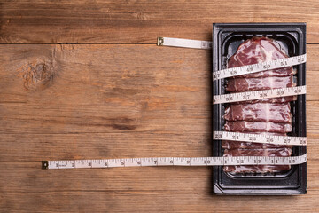 Fototapeta Pack of raw sliced Dry Aged beef in black plastic tray and waist tape on wooden table background. Food and healthcare concept obraz