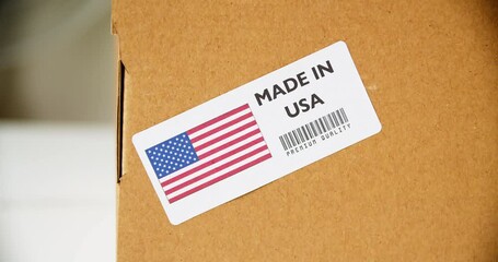 Hands applying MADE IN USA flag label on a shipping cardboard box with products. Close up shot with premium quality barcode. - Powered by Adobe
