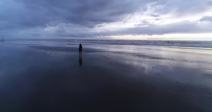 Drone aerial view. Silhouettes of a girl walking on the wide, big beach