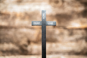 trust hope love text on black wooden cross with wooden blurred out background. jesus and religion concept.