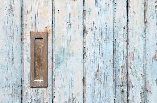 close up of an old wooden door with blue faded paint and a rusty closed old metal brass letterbox