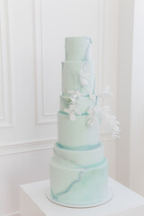 A large three-tiered wedding cake. The cake is covered with mastic of light green color in the form...