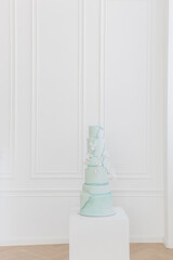 A large three-tiered wedding cake. The cake is covered with mastic of light green color in the form of stone marble. Decorations in the form of white rice paper flowers on a white background. Artistic