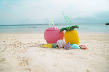 Exotic tropical summer drinks in pink shell shaped and pineapple shaped  bottle with colorful sea shells on the sandy beach background, Maldives