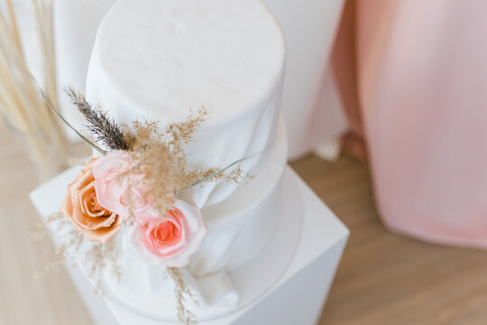 An elongated modern white wedding cake covered in mastic. Decorations in the form of flowers. Artistic decoration.Image for menu or catalog of confectionery.
