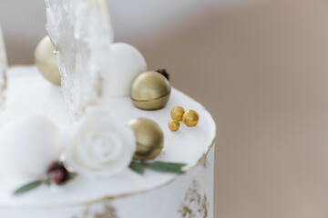 An elongated modern white wedding cake covered in cream and gold. Transparent heart-shaped lollipops. Artistic decoration.Image for menu or catalog of pastry shop.