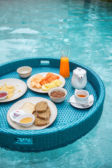 Floating breakfast in swimming pool. Healthy breafast served on the table relaxing in calm pool water, by tropical resort pool, summer beach luxury lifestyle