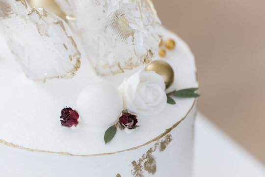 An elongated modern white wedding cake covered in cream and gold. Transparent heart-shaped lollipops. Artistic decoration.Image for menu or catalog of pastry shop.