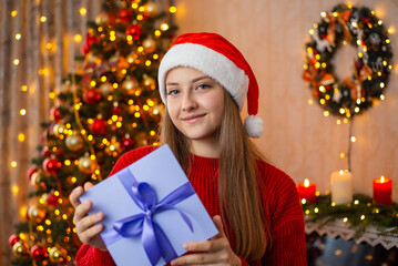 Young teenage girl holds Christmas present box in decorated living room. Christmas present concept