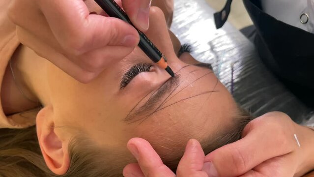 Cosmetologist drawing right shape of eyebrows during permanent makeup process