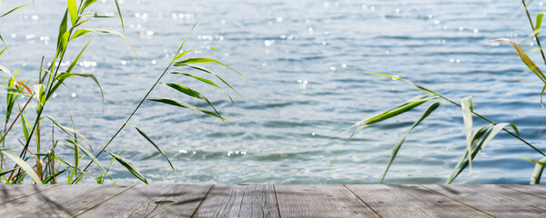wooden dock lakeside in sunshine, blurred water with sun lights behind empty wooden planks for...