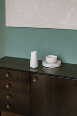 Mid-century modern furniture with decor. Close up. Interior elements. Wooden chest and ceramics near green wall.