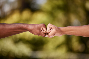 Fist bump of two interracial men outdoor against a blur background. Closeup of diverse athletes doing social gesture greeting in a park. Showing solidarity, friendship, brotherhood, teamwork or unity