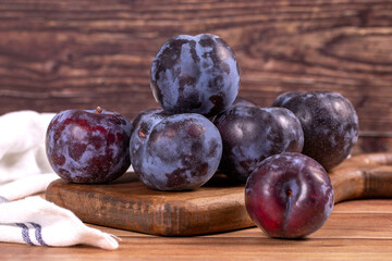 Black plum on wood background. A pile of black plums on a wood serving dish. close up