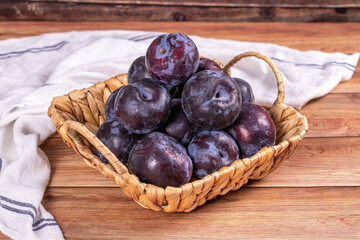 Black plum on wood background. A pile of black plums in a basket. close up