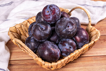 Black plum on wood background. A pile of black plums in a basket. close up