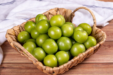 Green plum on wood background. A pile of green plums in a basket. close up