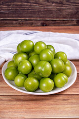 Green plum on wood background. Pile of green plums on a white serving plate. close up