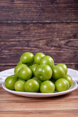 Green plum on wood background. Pile of green plums on a white serving plate. close up