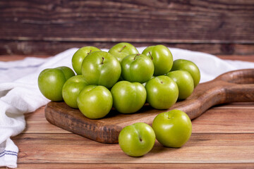 Green plum on wood background. Pile of green plums on wooden serving plate. close up