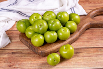 Green plum on wood background. Pile of green plums on wooden serving plate. close up