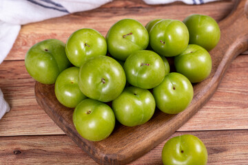 Green plum on wood background. Pile of green plums on wooden serving plate. close up