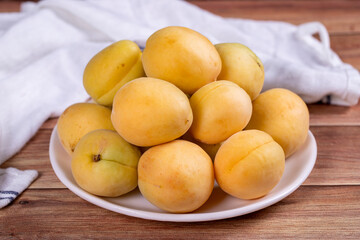 Apricots on wood background. Pile of fresh apricots in a white plate. close up