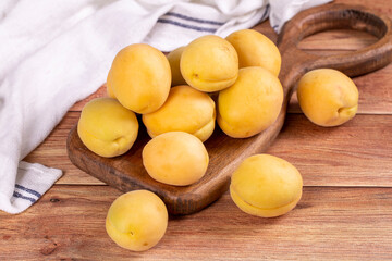Naklejka na ściany i meble Apricots on wood background. Stack of fresh apricots in a wooden serving plate. close up