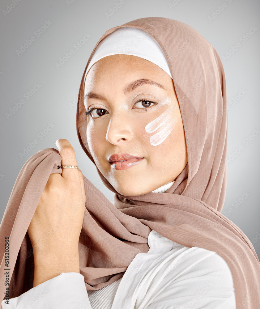 Wall mural portrait of a muslim woman using face moisturiser, sunscreen or lotion isolated on a grey studio bac