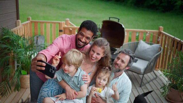 Family with kids having fun at barbecue party dinner on patio, people sitting and taking selfie.