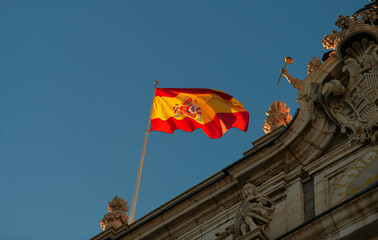 Flag of Spain winding in sunset light against blue sky on top of Royal Palace building from Madrid.