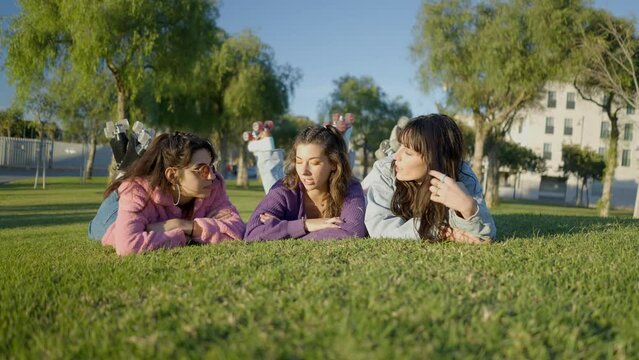 Teenage girls lie face down on grass and talk, frontal ground view
