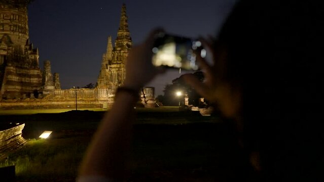 Traveler girl in mask takes a picture of Wat Yai Chai Mongkhon temple in Ayutthaya at night, Thailand